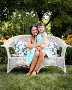 young mother and daughter on a sofa under trees in a beautiful garden