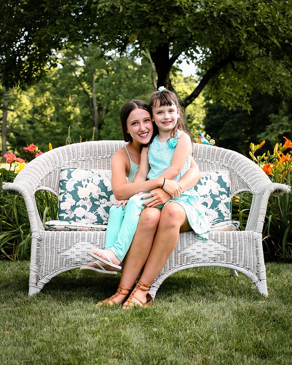 young mother and daughter on a sofa under trees in a beautiful garden